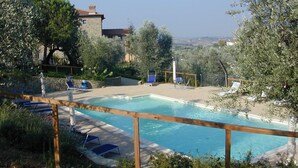 Una piscina con sillones de descanso y un edificio de piedra al fondo.