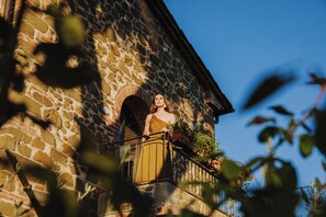 A person standing on a balcony with a stone building in the background.