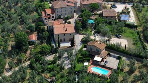 Vista aérea de una zona rural con olivares en terrazas, edificios de piedra con tejados de tejas rojas y una piscina.
