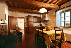 A rustic kitchen with wooden cabinets, a dining table with chairs, and a hanging light fixture.