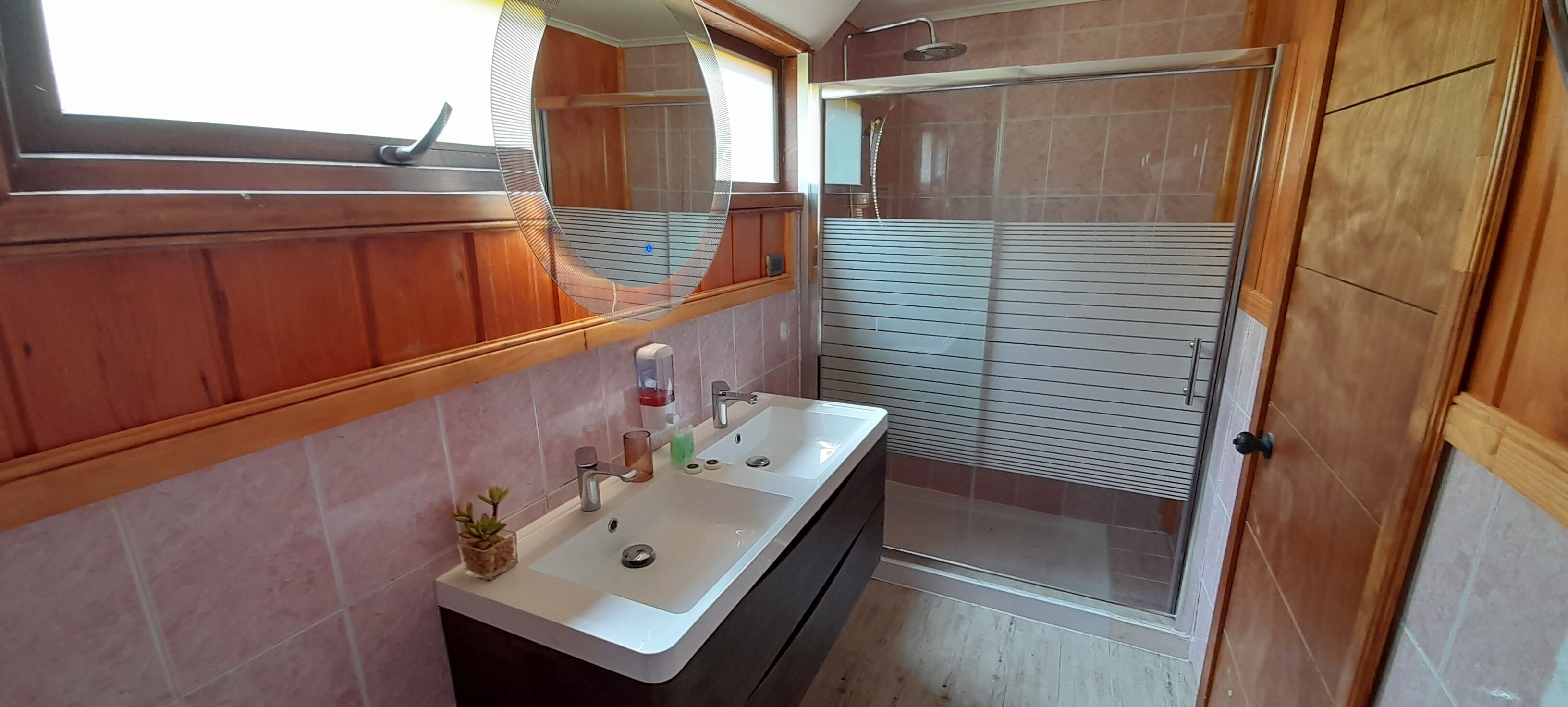 A bathroom with a wooden vanity, a sink, a mirror, and a shower area.