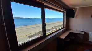 A room with a large window overlooking a beach, a small table, and a radiator on the wall. - Hotel CasaQuinchao (Isla Quinchao)