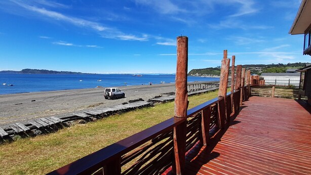 A wooden deck with a view of the beach and ocean. - Hotel CasaQuinchao (Isla Quinchao)