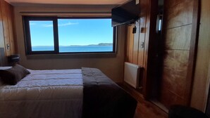 A bedroom with a large bed, a window with a view of the sea, and wooden walls. - Hotel CasaQuinchao (Isla Quinchao)