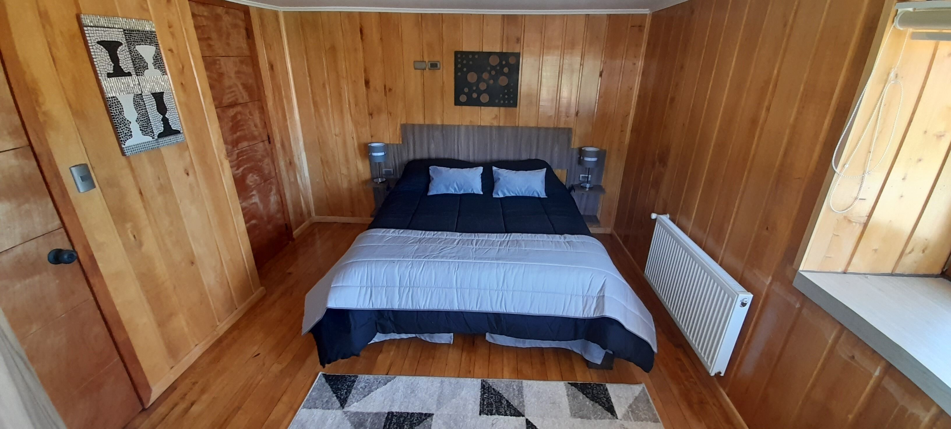 A bedroom with a bed, wooden walls, a radiator, and a rug.