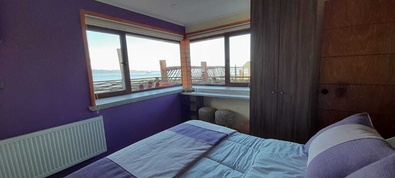 A bedroom with a bed, a window with a view of the sea, and a wooden door.