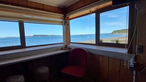 A room with large windows overlooking a beach, a red chair, and a wooden interior. - Hotel CasaQuinchao (Isla Quinchao)