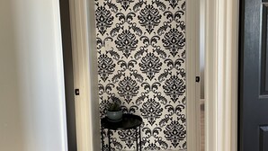 A hallway with a patterned wallpaper, a small table with a potted plant, and a door on the right.