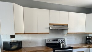 A modern kitchen with white cabinets, a wooden countertop, a black microwave, a stainless steel stove, and a coffee maker.