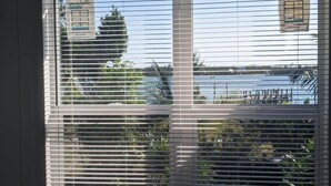 A window with horizontal blinds, a view of a body of water, and a building with a sign in the background.