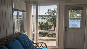 A room with a blue sofa, a door leading outside, and a view of a beach and palm trees.