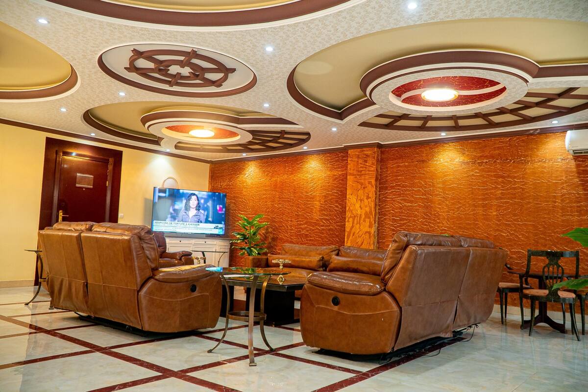 Un hall con sofás de cuero, una televisión y un techo decorativo.