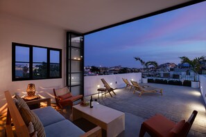 A rooftop terrace with a seating area, a table with a bottle and glasses, and a view of the cityscape at dusk. - Amazing Roof Top Views, 5 Minute Walk From The Beach. Centro Historico (Mazatlán)