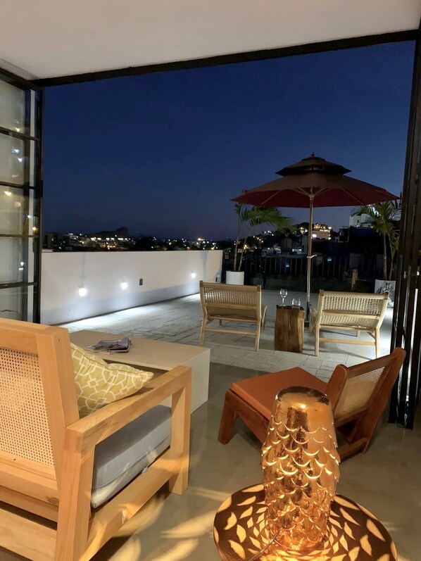 A rooftop terrace with wicker furniture, a table with a decorative lamp, and an umbrella.