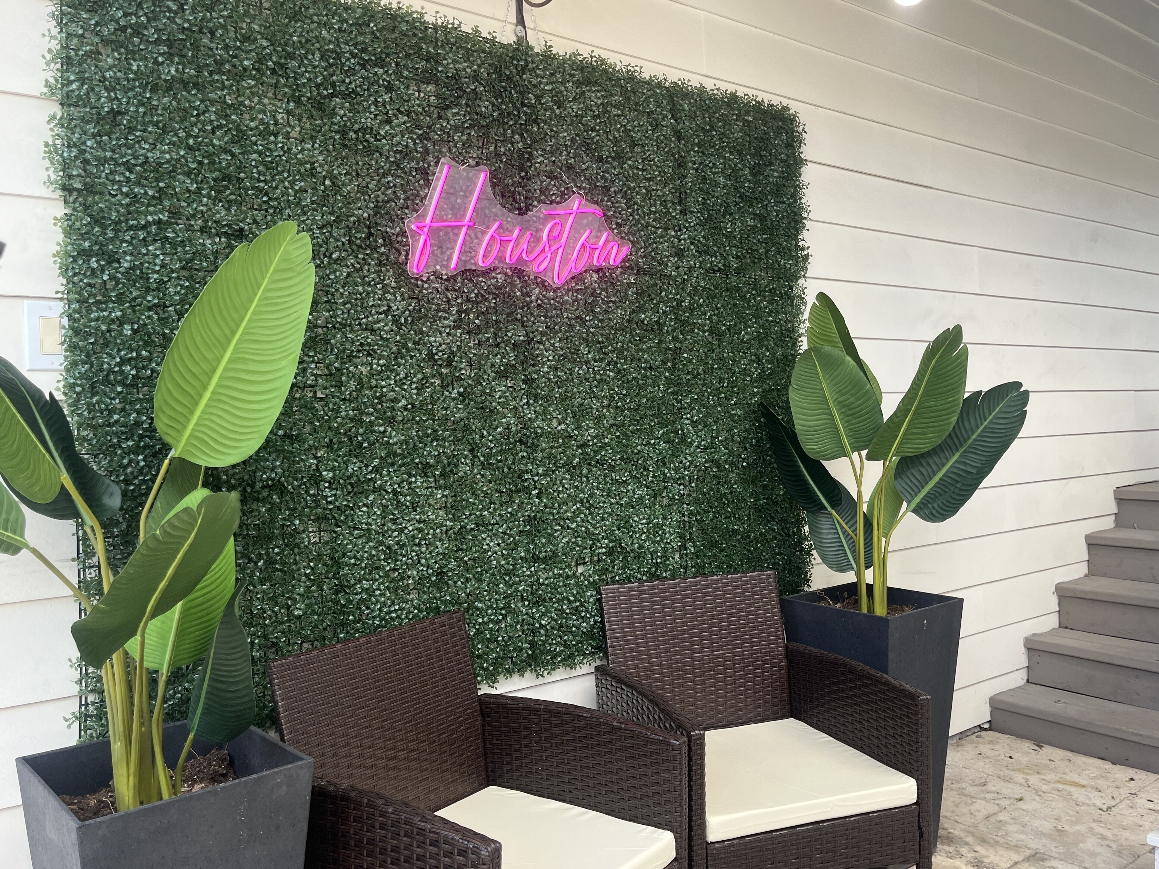 A seating area with wicker furniture and a green wall with a neon sign reading "Houston."