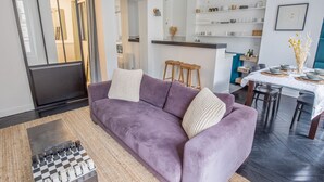 A modern living room with a purple sofa, a chess table, and a kitchen area in the background.