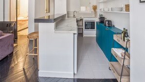 A compact kitchen with a central island, a dining area with a purple sofa, and a view into a bedroom.