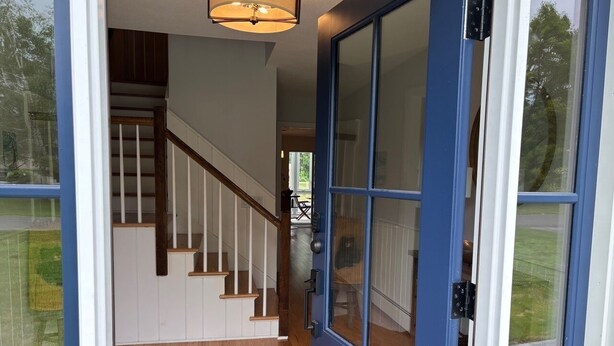 A blue door with glass panels, a wooden staircase, and a patterned rug leading to a room. - Lenox Grand Colonial with Pool by Evergreen Home (Lenox)