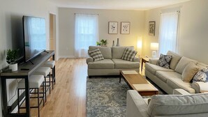 A modern living room with a sofa set, a coffee table, a TV, and a small bar area. - Lenox Grand Colonial with Pool by Evergreen Home (Lenox)