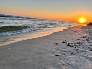 A beach at sunset with waves, sand, and scattered debris.
