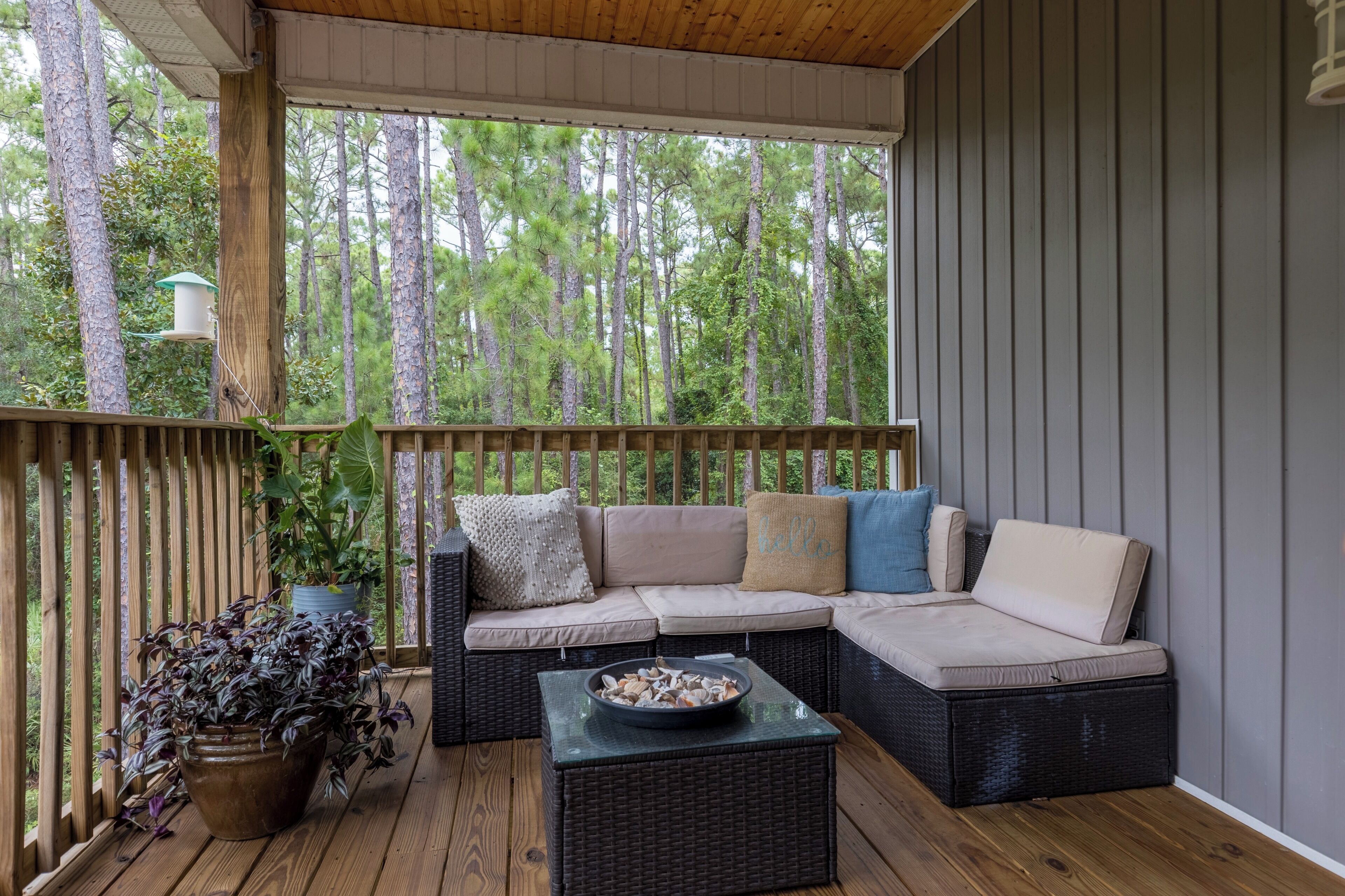 A covered outdoor seating area with a wicker sofa, a small table, and potted plants.