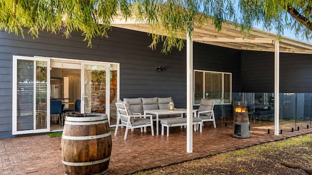 An outdoor patio with a covered seating area, a fire pit, and a wooden barrel.