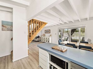 A modern kitchen with a wooden staircase, a dining area with a large window, and a view of the outdoors.