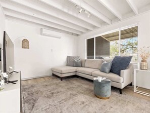 A modern living room with a sectional sofa, a round coffee table, and a large window with blinds.