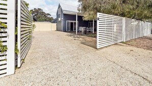 A residential property with a gravel driveway, a covered outdoor seating area, and a fenced garden.