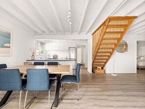 Un vaste espace de vie comprenant une table à manger, des chaises bleues, une cuisine en arrière-plan et un escalier en bois.