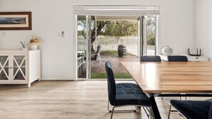 A modern interior with a wooden dining table, black chairs, a white cabinet with glass doors, and a sliding glass door leading to an outdoor patio.
