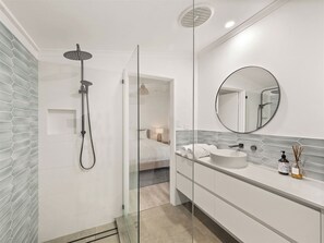 A modern bathroom with a glass-enclosed shower, a round mirror, and a white sink with a soap dispenser.