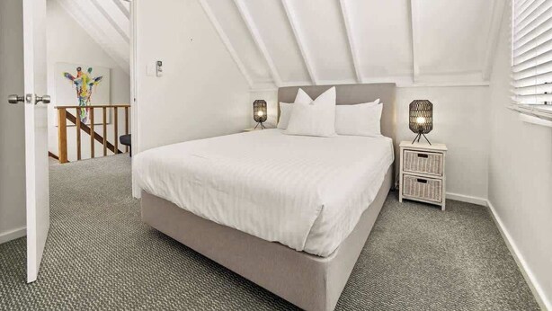 Une chambre à coucher avec un grand lit, deux tables de chevet, une commode et une porte donnant sur un escalier.