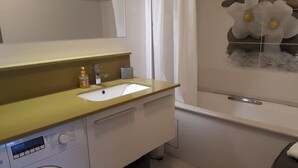 Un baño pequeño con lavadora, lavamanos y zona de ducha.
