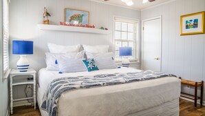 A bedroom with a bed, two bedside tables, a ceiling fan, a window with blinds, and a door. - Gulf Front!! 2 Master Suites- Steps Away from the Beach!! (Dauphin Island)