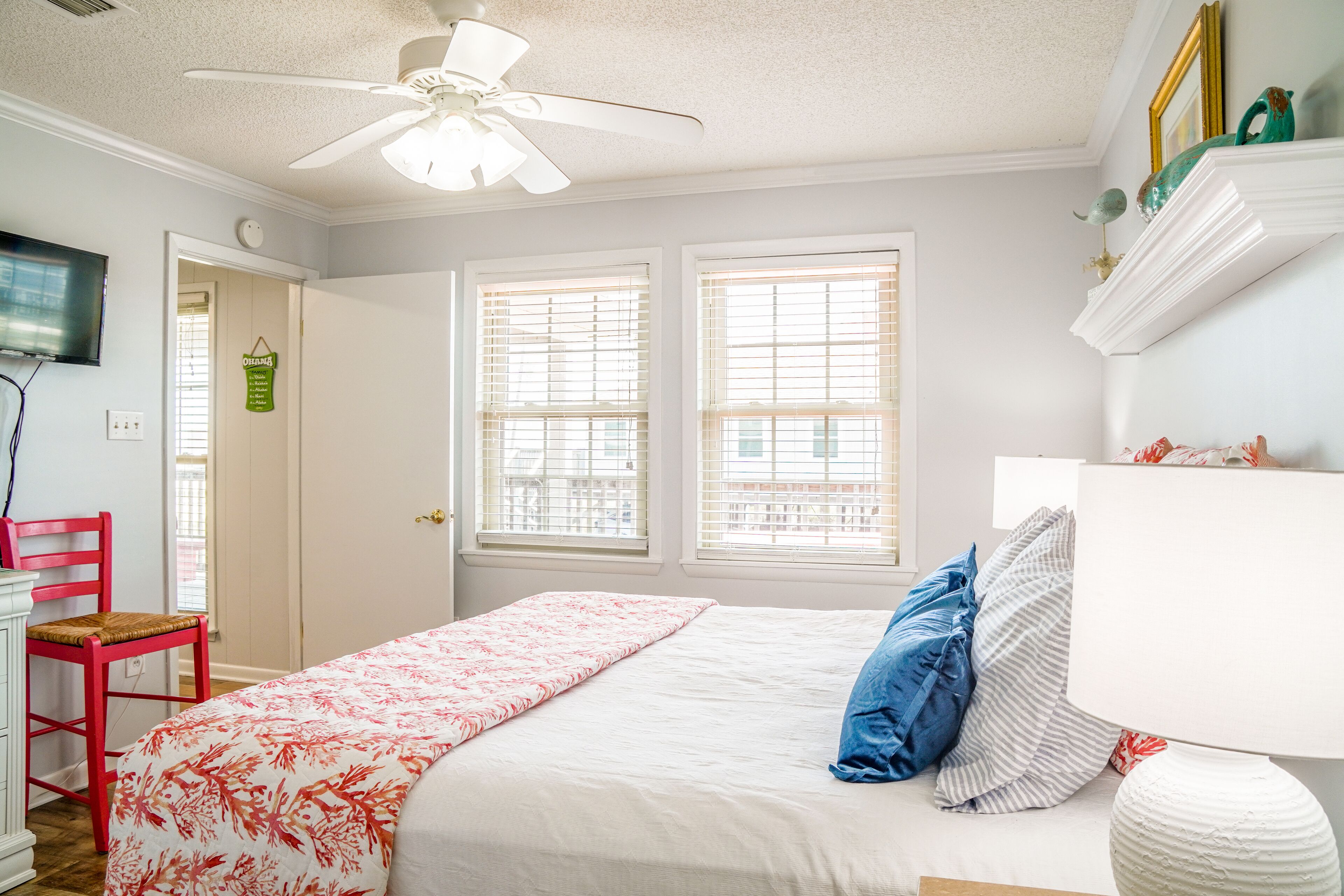 Ein Schlafzimmer mit Bett, Sessel, Deckenventilator und Fenstern.