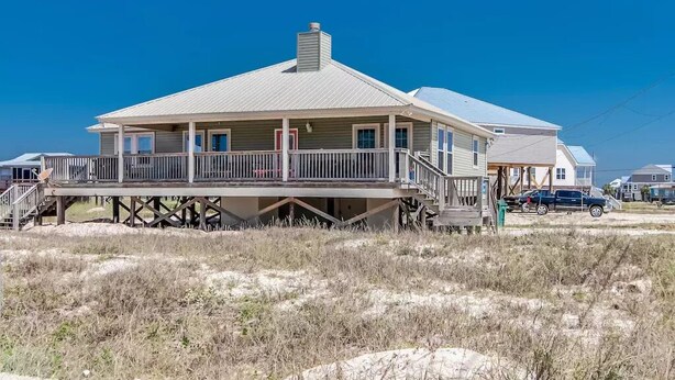 A two-story house with a balcony, situated on stilts over a sandy area. - Gulf Front!! 2 Master Suites- Steps Away from the Beach!! (Dauphin Island)