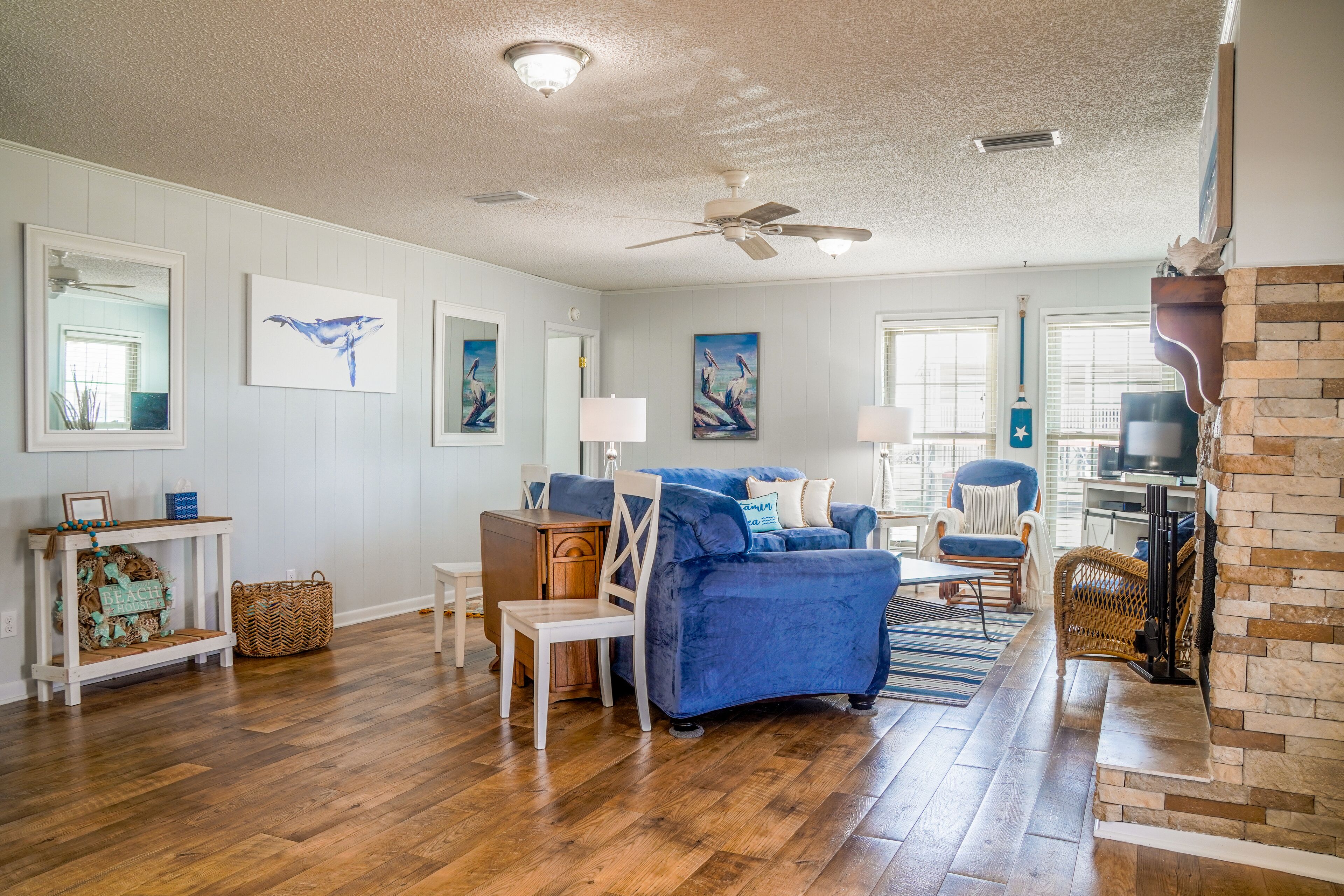 A spacious living room with hardwood flooring, a blue sofa, a fireplace, and artwork on the walls.