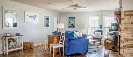 A spacious living room with hardwood flooring, a blue sofa, a fireplace, and artwork on the walls.