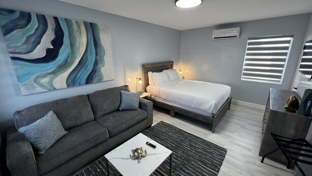 Et moderne hotelværelse med en grå sofa, en hvid seng, et marmorbord og et stort abstrakt maleri på væggen.