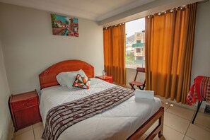 A neatly made bed with a patterned blanket, a wooden headboard, a small bedside table, and a nightstand. - ALO INKA HOTEL (Cusco)