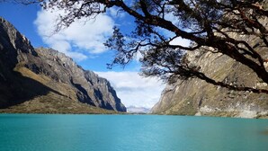 Un lago sereno rodeado de montañas escarpadas, con cielos despejados y una rama destacada en primer plano.