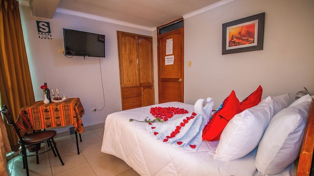 Habitación de hotel con cama, televisor, escritorio y silla, y una puerta.