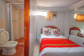A hotel room with a shower, toilet, two beds with red and white bedding, and a window with curtains. - ALO INKA HOTEL (Cusco)