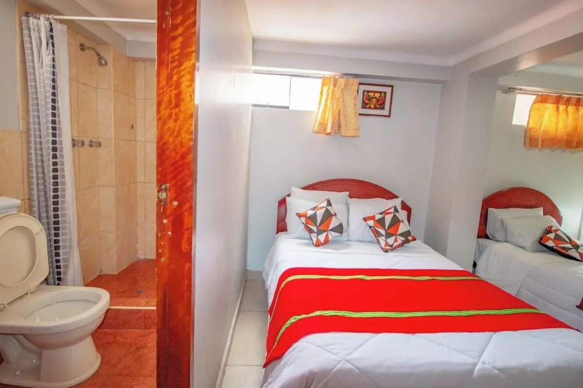 Habitación de hotel con ducha, inodoro, dos camas y ventana con cortinas.
