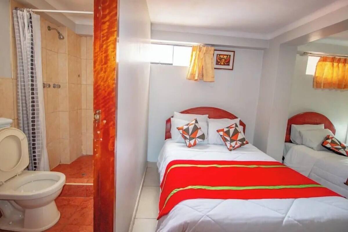 Habitación de hotel con ducha, inodoro, dos camas y ventana con cortinas.