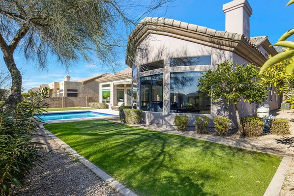 Uma casa moderna com piscina, gramado bem cuidado e céu azul límpido.