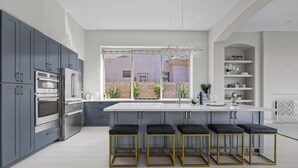 Una cocina moderna con gabinetes grises, electrodomésticos de acero inoxidable y una isla central con taburetes de bar.