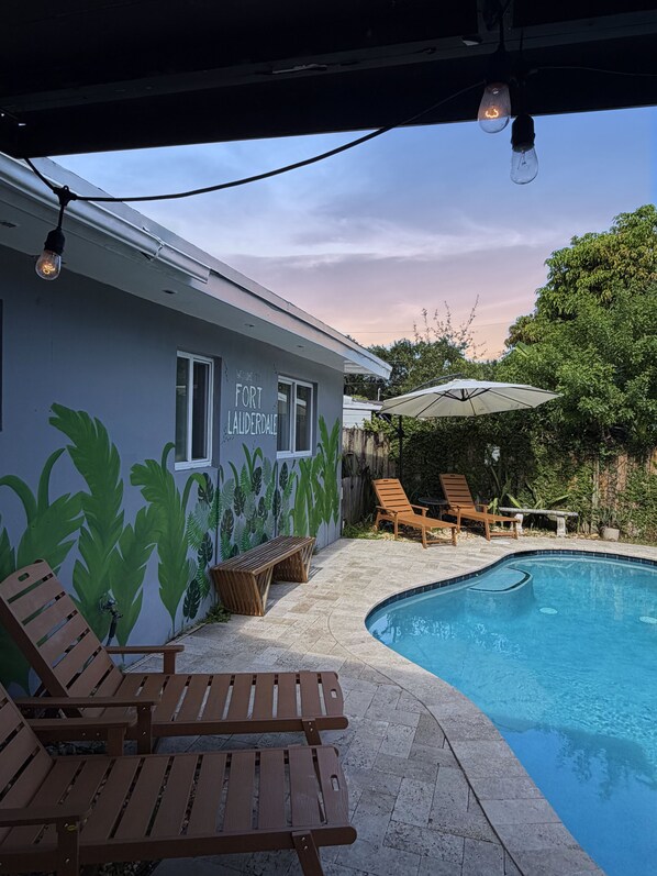 A poolside area with lounge chairs, a pool, and a building with a mural.