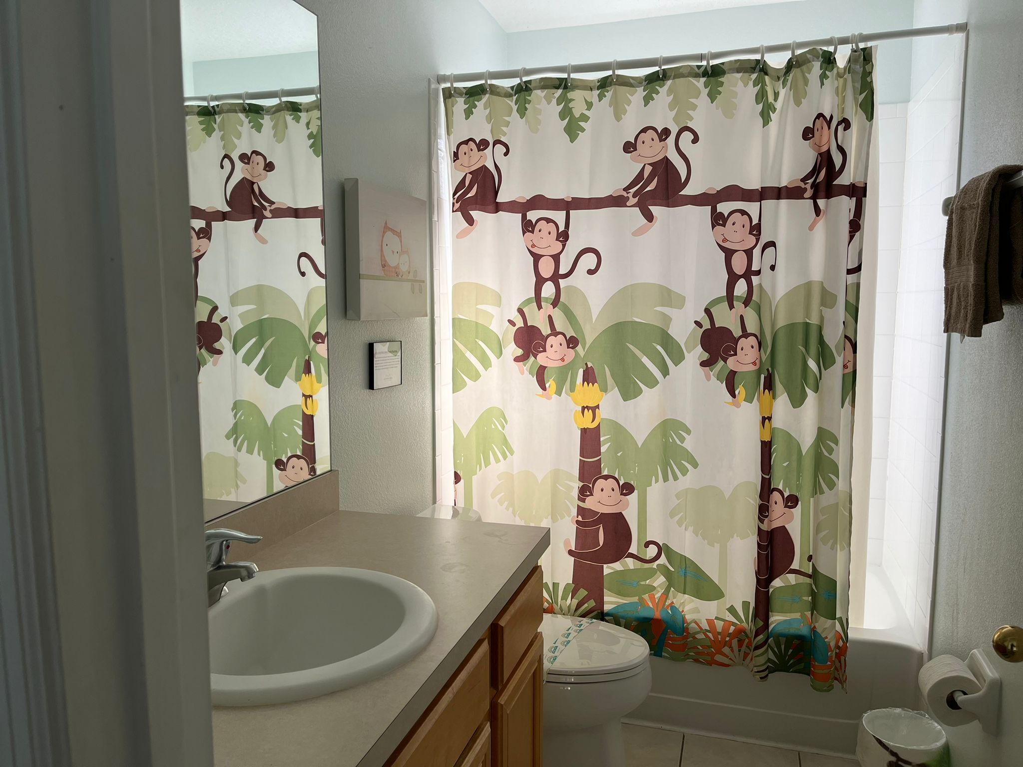 A bathroom with a toilet, sink, and shower curtain featuring monkey and plant designs.